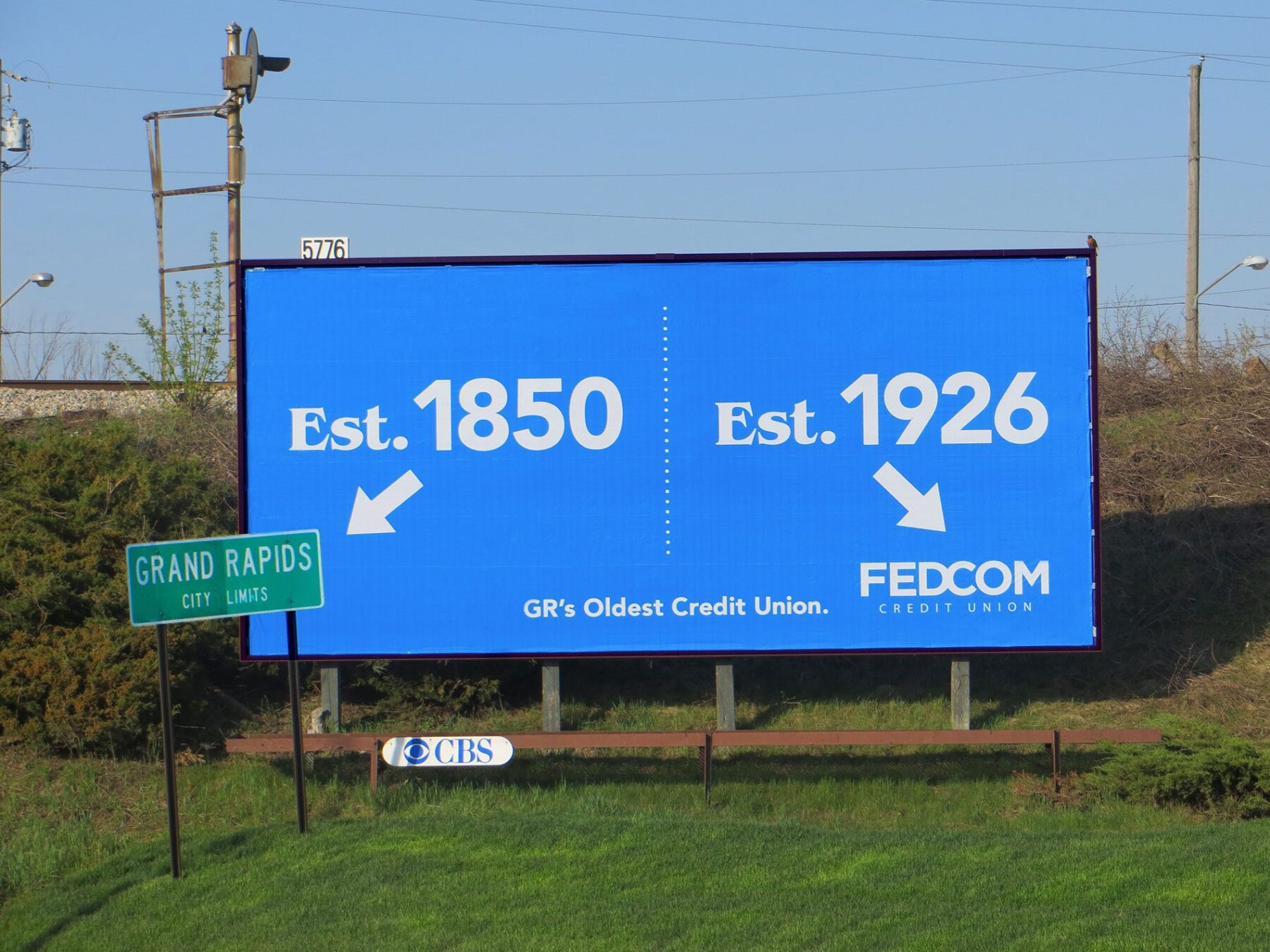 Billboard for Fedcom Credit Union. “Est. 1850” with an arrow pointing to the Grand Rapids City Limits sign. “Est. 1926” & the Fedcom logo.