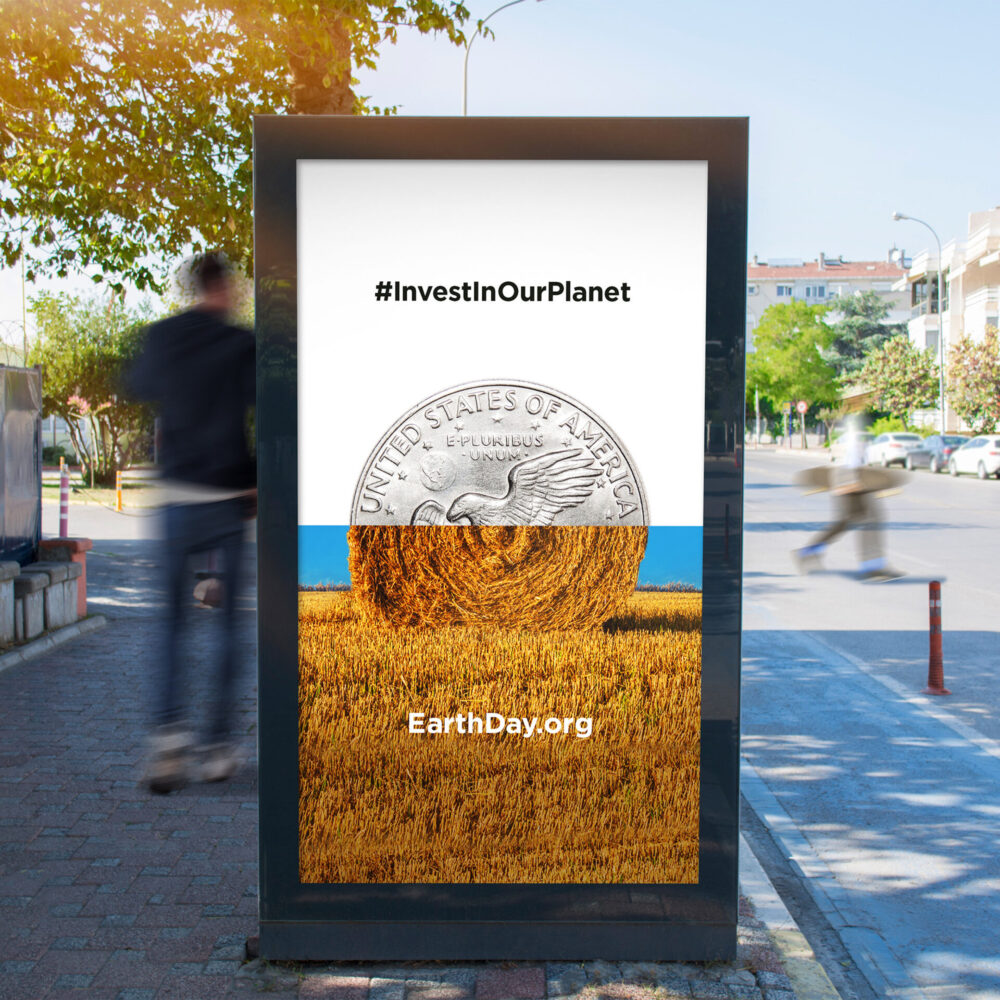 Out of home advertising bus station kiosk with #InvestInOurPlanet and image of a coin aligned with a hay bale