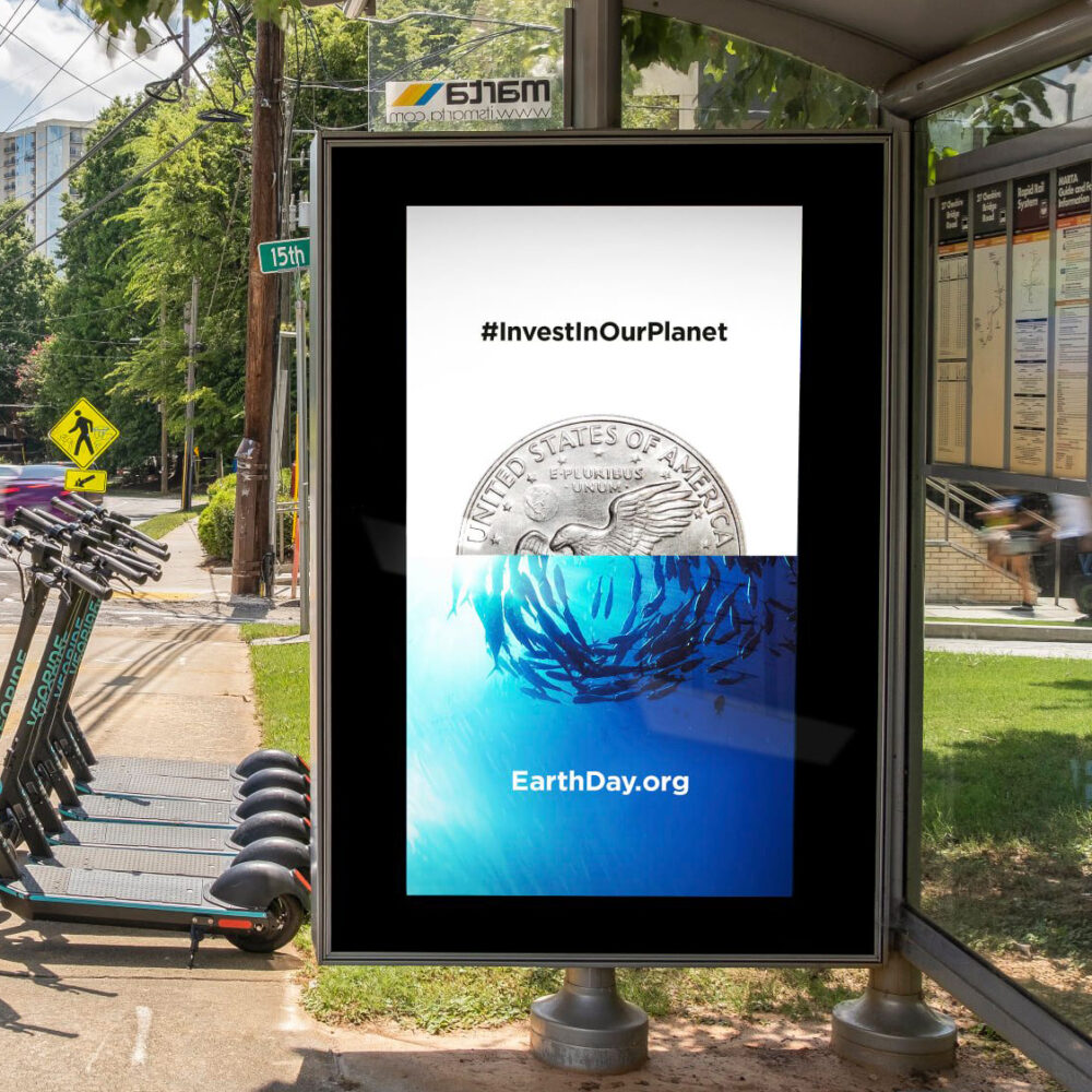 Out of home advertising bus station kiosk with #InvestInOurPlanet and image of a coin aligned with a wave of water.