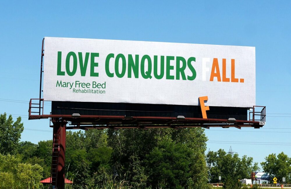 Billboard featuring the headline, “Love Conquers (F)All” The ‘F’ appears to have fallen off the board so that the word reads “all.”