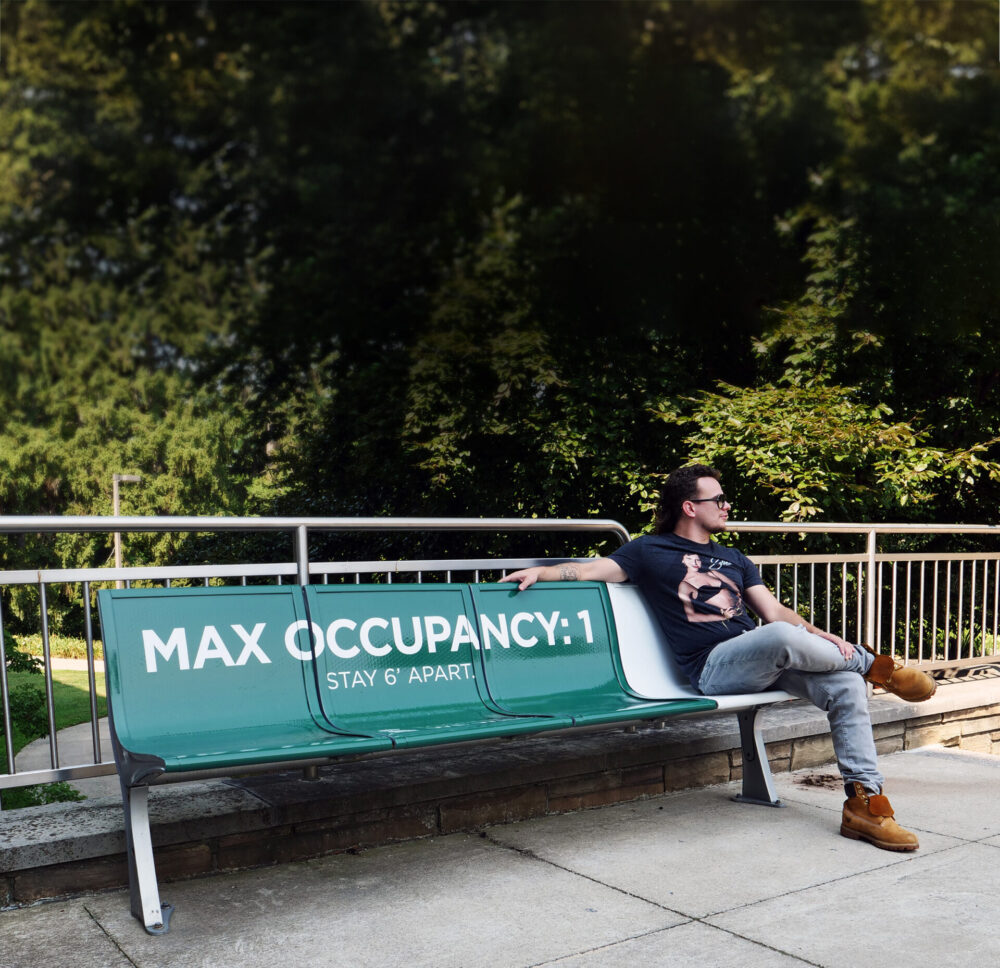 Man sitting on a bench with a decal saying "Max occupancy: 1"