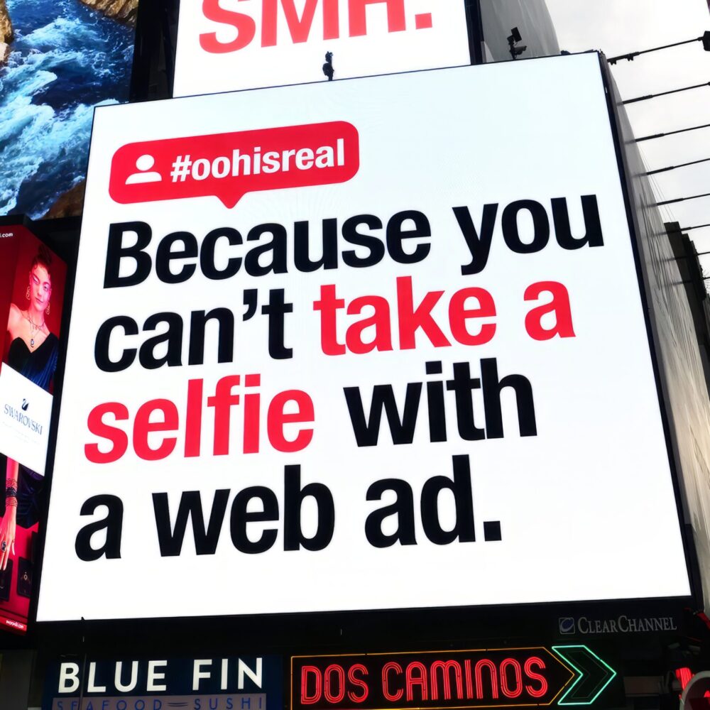 Digital out of home advertisement in Times Square with "Because you can't take a selfie with a web ad."