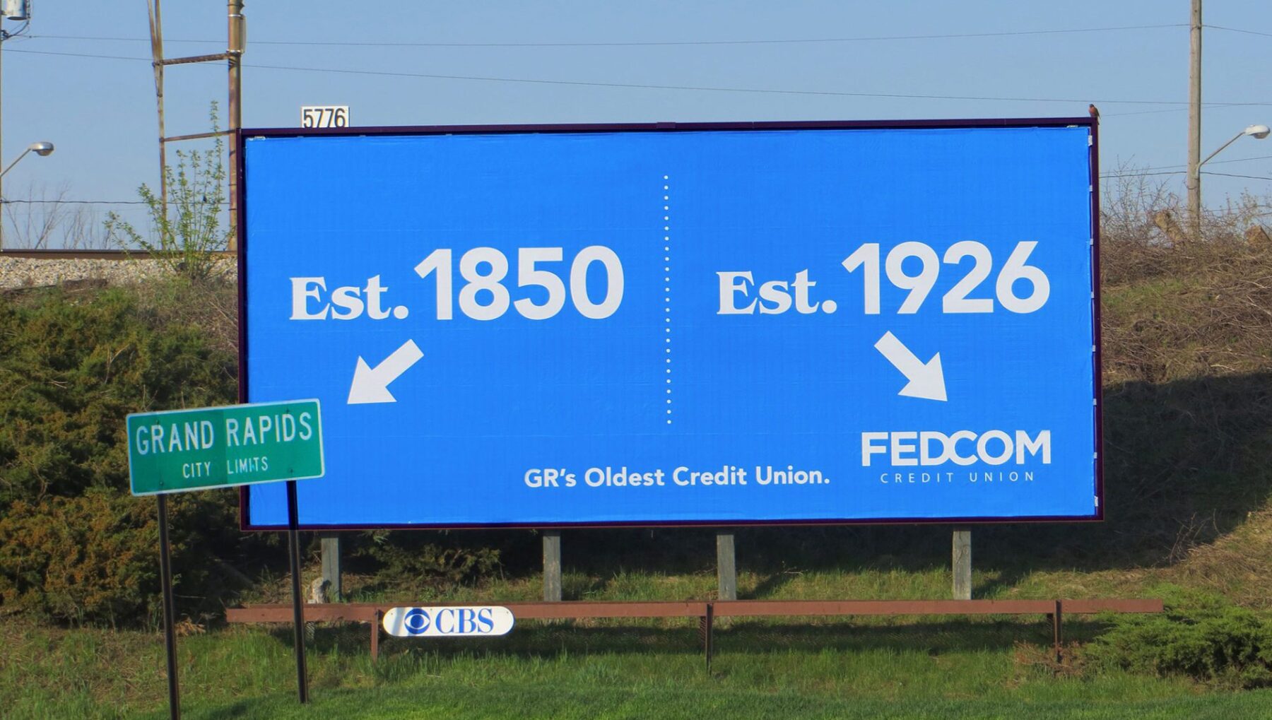Established 1850 points to a street sign saying "Grand Rapids City Limits" and Est. 1926 pointing to the FEDCOM Credit Union logo.