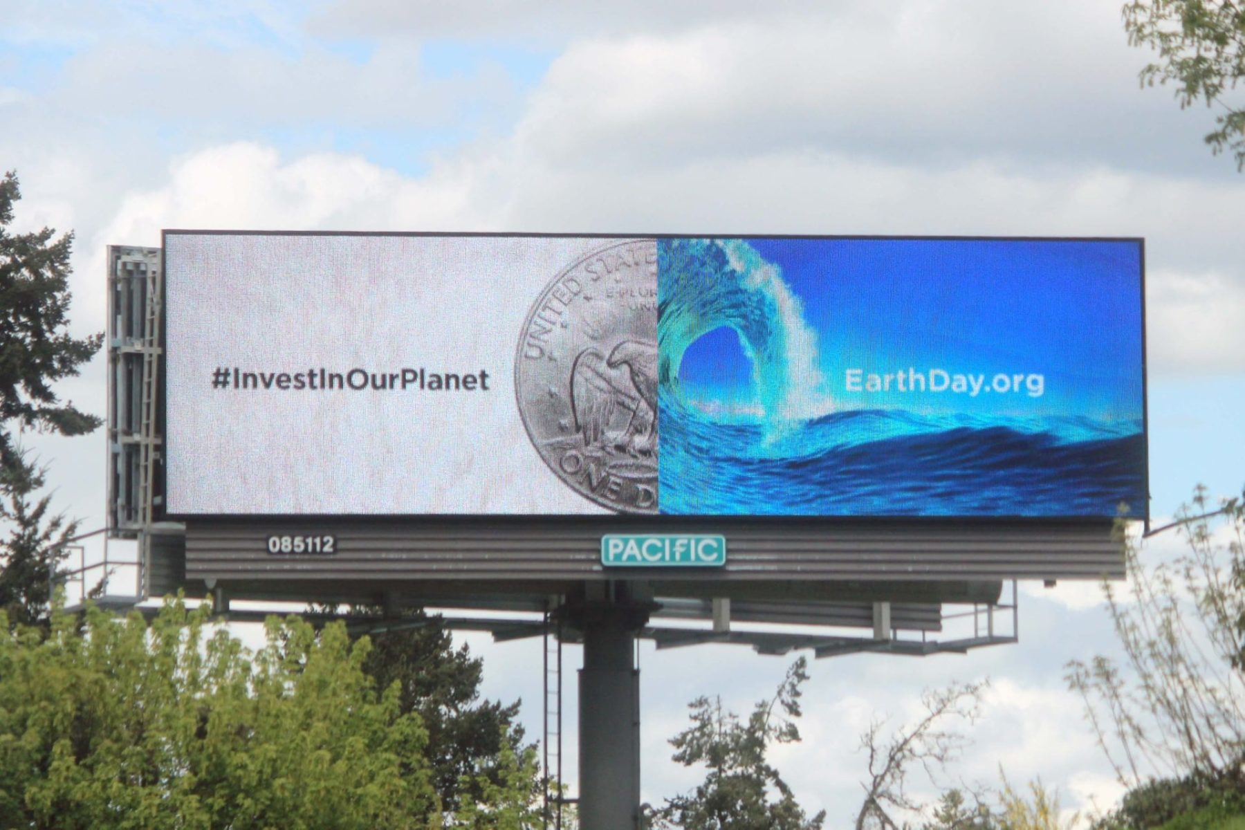 Out of Home Advertising digital billboard with #InvestInOurPlanet and image of a coin aligned with a wave of water.