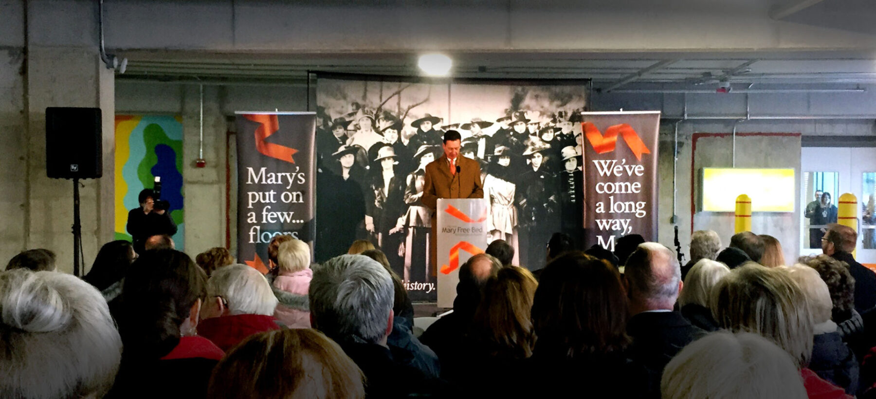Mary Free Bed Rehabilitation Grand Reopening Ceremony with banners and the headlines, “Mary’s put on a few… floors,” & “We’ve come a long way,”