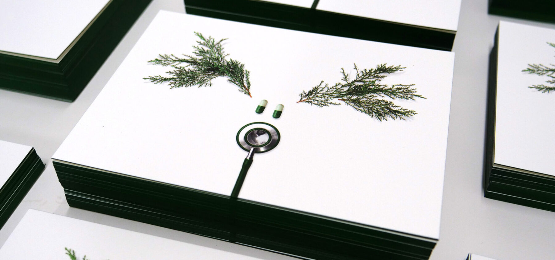 Stacks of holiday postcards with design of reindeer created from a stethoscope, two pills and some evergreen branches