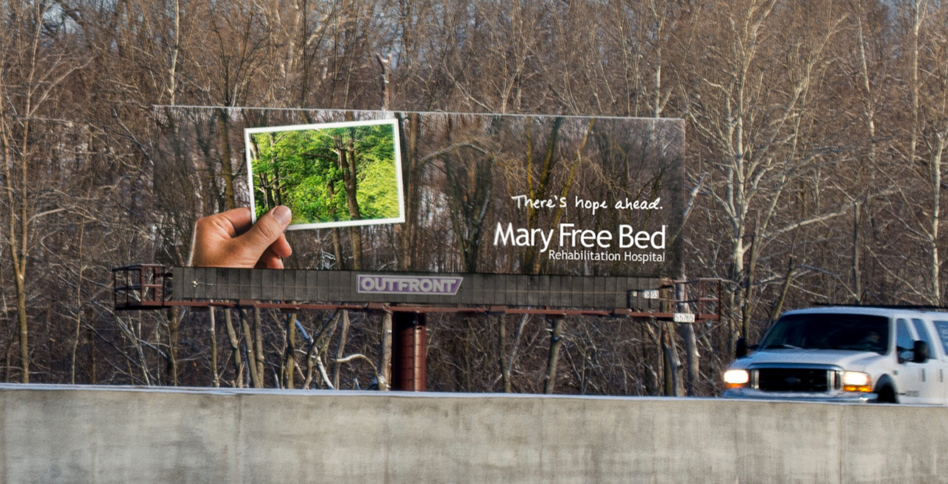 Billboard featuring bare trees in winter, with a hand holding an image of trees in full bloom, with the headline, “There’s hope ahead.”