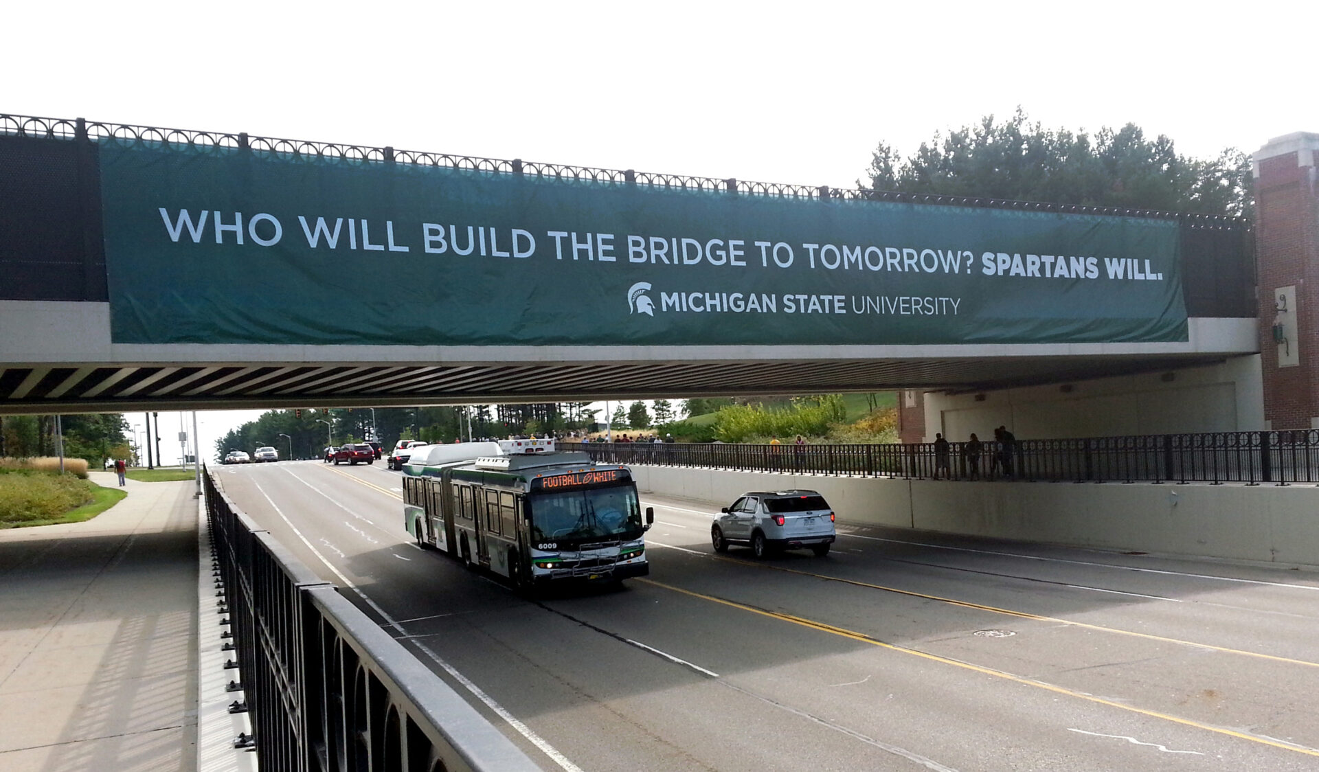 Michigan State University Exterior Banner hanging on overpass with headline "Who will build the bridge to tomorrow? Spartans Will."