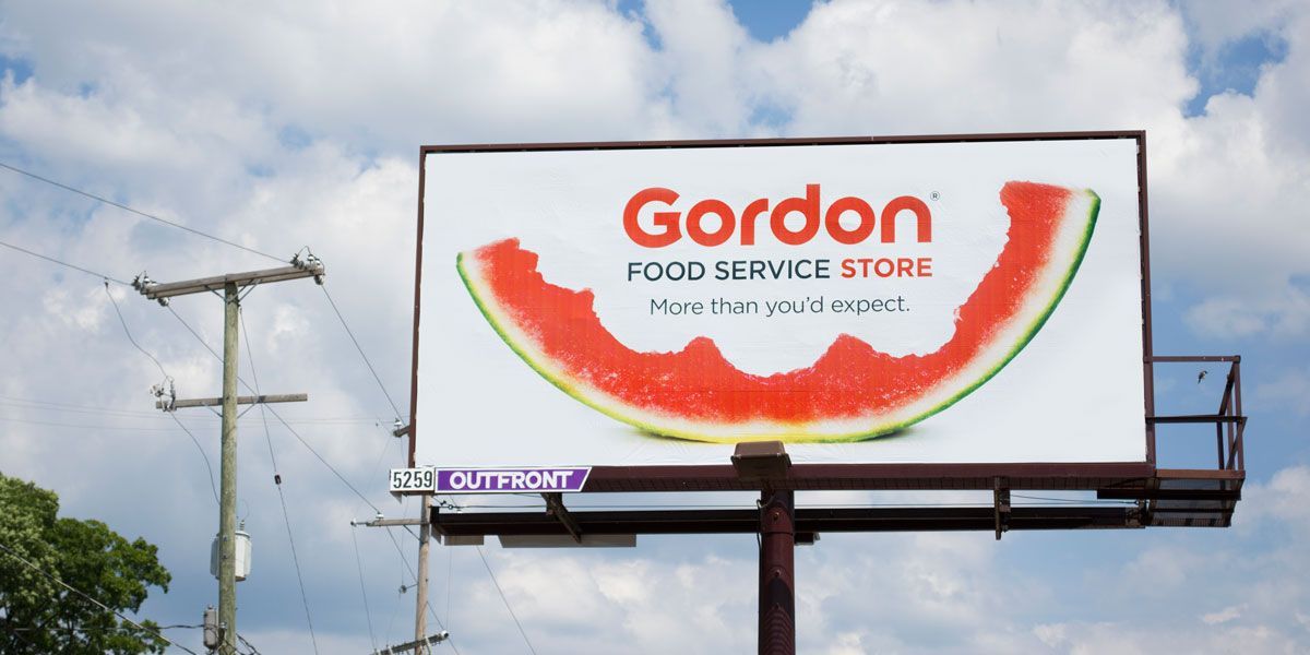 Billboard for Gordon Food Services of a slice of watermelon with bites taken out, the GFS logo, & the headline, “More than you’d expect.”
